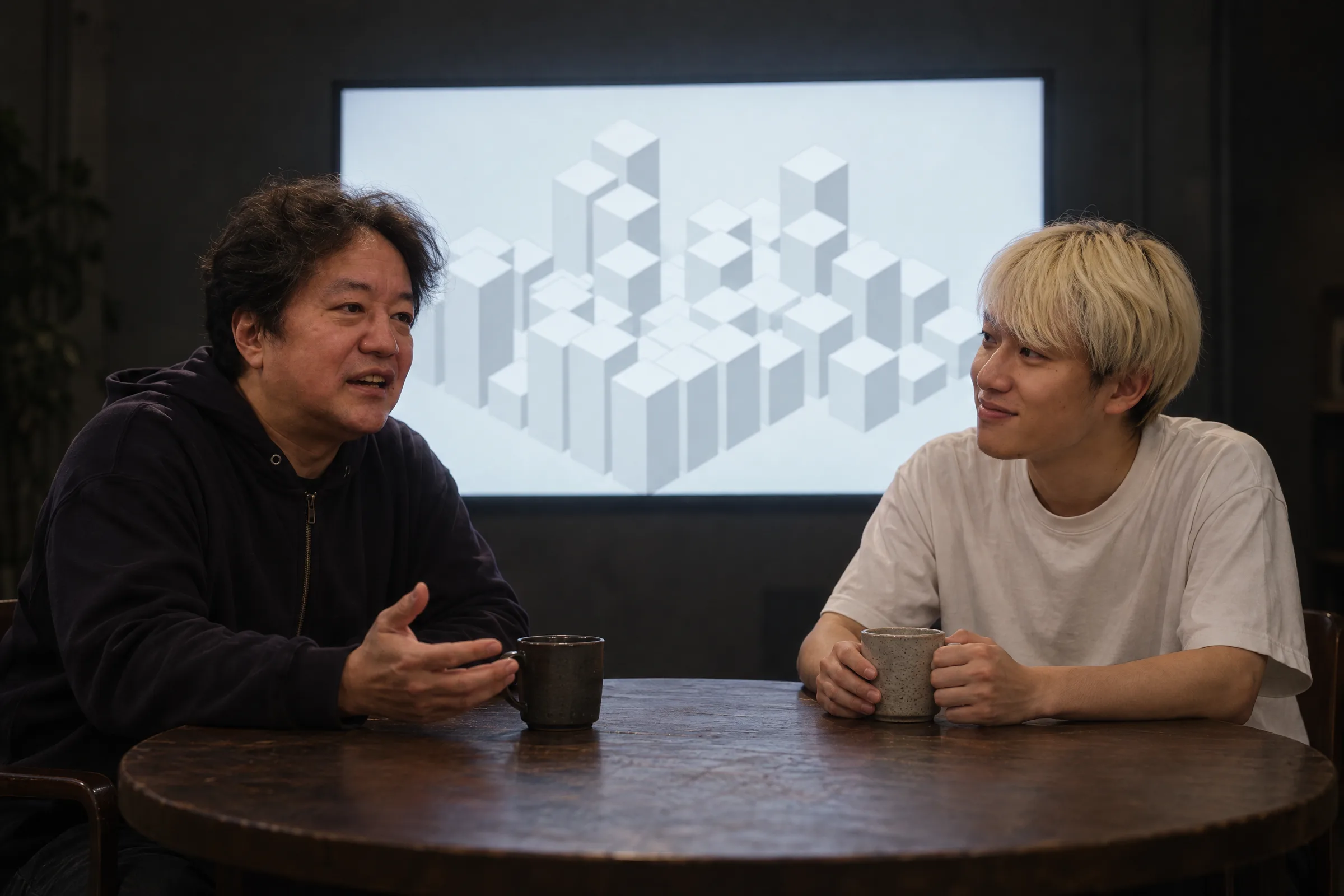平野友康と野口岳が、CITY の街が映った画面の前で話している