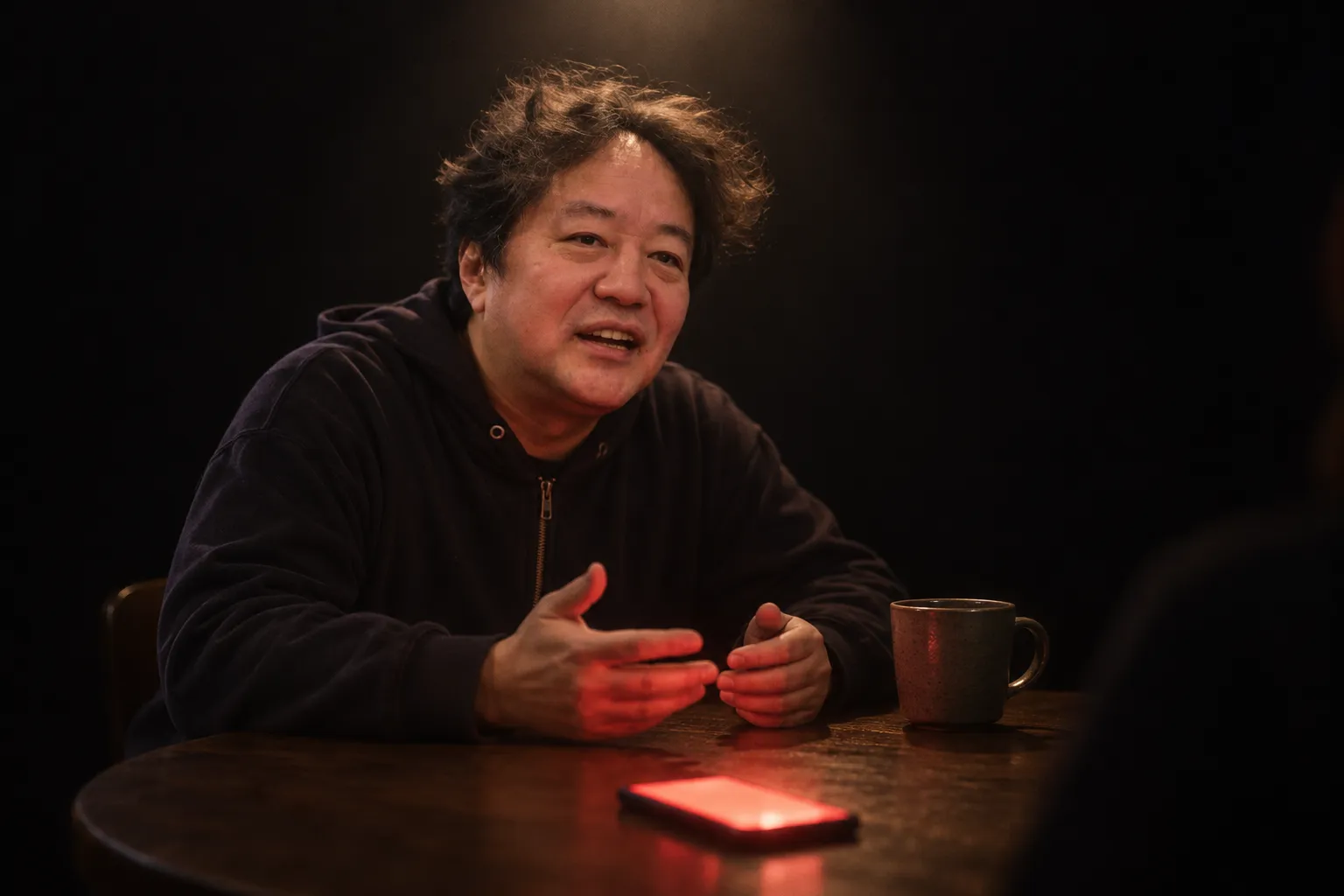 円卓で話す平野。手元のスマホが赤く光っている